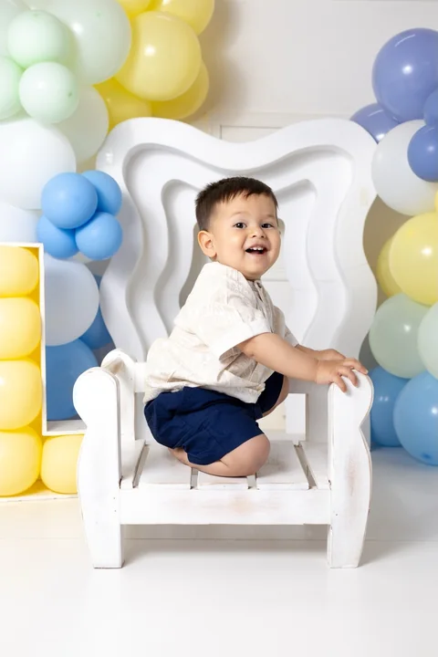 Bebé sonriente en una silla blanca con globos de colores